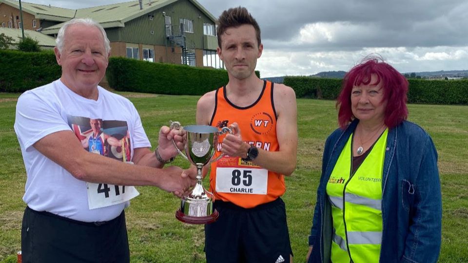 Jon Ward 5K winner Charlie Jones being presented with his trophy by Trevor Ward