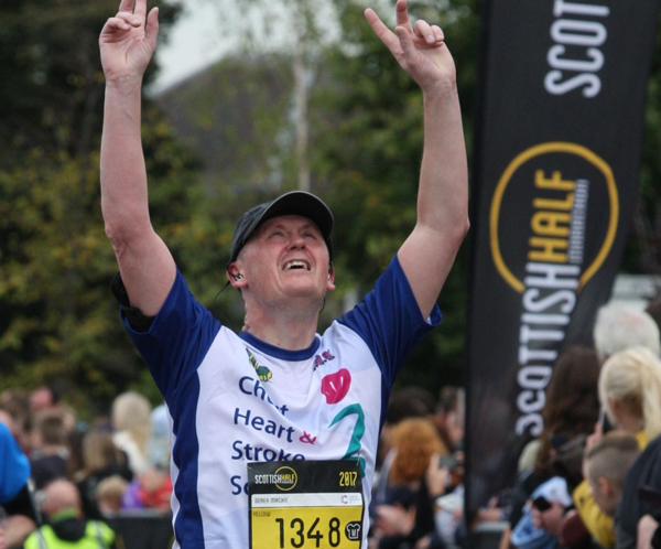runner in CHSS vest raises his arms after finishing Scottish Half Marathon