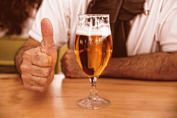 Man with thumbs up beside a glass of beer on table top