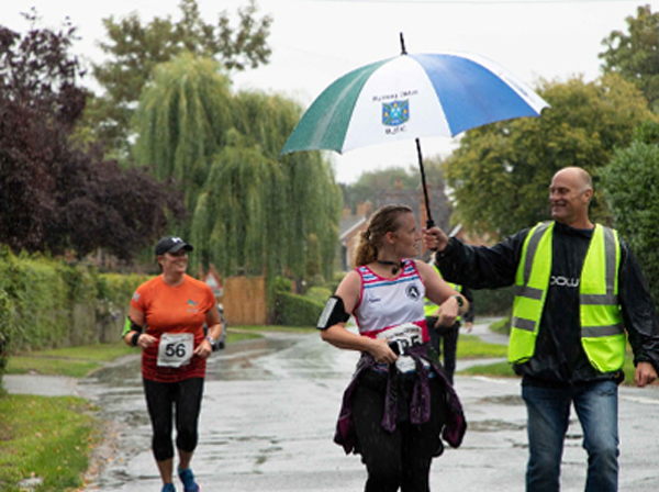 Man with umbrella shelters runner in race